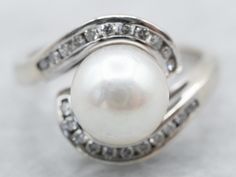 "What an elegant combination of colors! We love the way this vintage cocktail ring evokes the past, like a 1920's dress that flows with cream satin and sparks with sequins. This is a lovely pearl, a velvety gem with a sophisticated color! The setting is white gold, a swirling take on the classic bypass style, studded with diamond accents! Metal: 14K White Gold Gem: Pearl Gem Measurements: 8.0 mm, Round Accents: 22 Diamonds totaling .22 Carats, H in Color, SI1 in Clarity Ring Size: 5.75 Marks: \" White Gold Pearl Ring, 1920's Dress, Pearl Anniversary, Petite Earrings, Gold Pearl Ring, Vintage Cocktail Ring, Ring Pearl, Pearl And Diamond Ring, Bypass Ring