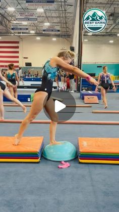 a woman standing on top of a blue mat in front of other women doing gymnastics