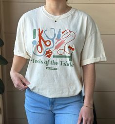 a woman wearing a t - shirt that says tools of the trade with scissors on it