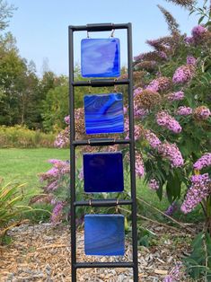 a sculpture made out of glass sitting on top of a metal stand next to purple flowers