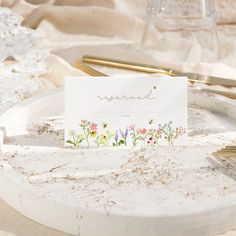 a place card is placed on a plate with gold forks and napkins next to it