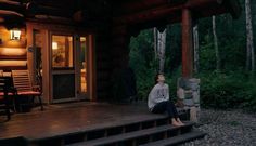 a woman sitting on the steps in front of a log cabin at night with her eyes closed