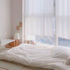 an unmade bed with white sheets and pillows in front of a window overlooking the city