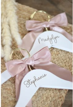 two personalized wedding hangers with pink bows and names on them, sitting on a woven mat