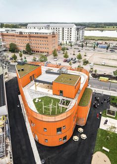 an orange building with green roof and grass on the top floor, surrounded by other buildings