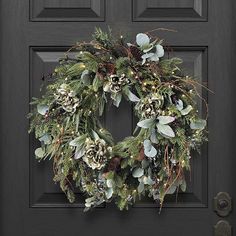 a wreath on the front door with pine cones and greenery hanging from it's sides