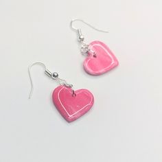 two pink heart shaped earrings with silver hooks on a white surface, one is dangling from the earwires