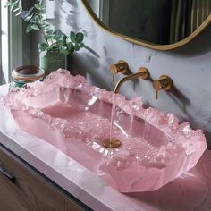 a pink sink with gold faucets in front of a mirror