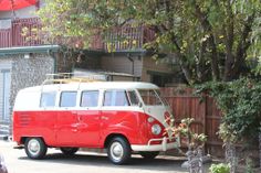 an old red and white van parked in front of a house next to a tree