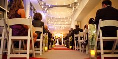 a group of people sitting on white chairs in front of a red carpeted aisle