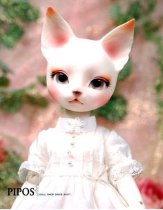 a close up of a doll wearing a white dress and cat's head with big eyes