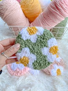 a hand holding a small crocheted flower pot holder in front of some yarn