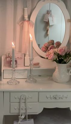 a white dresser with flowers and candles on it in front of a mirror that is lit