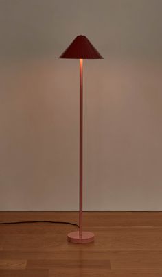 a floor lamp with a red shade on the base and a white wall behind it