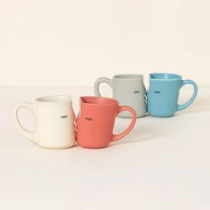 three different colored coffee mugs with eyes drawn on the side and one has eyelashes