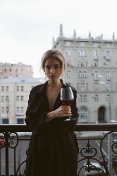 a woman holding a glass of red wine in her hand and looking at the camera