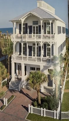 an aerial view of a large white house with palm trees in the foreground and ocean in the background