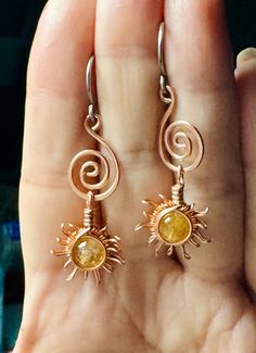 a pair of earrings that are on someone's hand with the sun in it