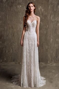 a woman in a white wedding dress standing against a gray wall with her long hair pulled back