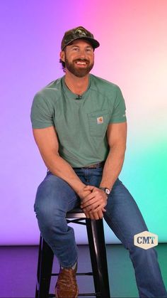 a man sitting on top of a stool in front of a colorful wall and smiling