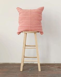 a pink pillow sitting on top of a wooden stool in front of a white wall