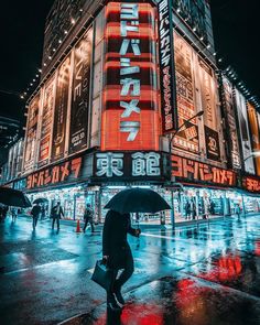 a person with an umbrella walking down the street at night in front of a building