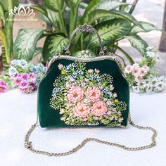 a green purse with pink flowers on it sitting on a table next to potted plants