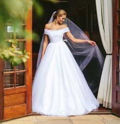 a woman in a white wedding dress is standing outside the door with her veil over her head