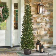 a christmas tree is on the front porch with two lanterns and a wreath hanging over it