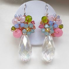 a pair of earrings with colorful stones and flowers on them sitting on a white surface