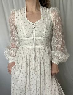 Details: maxi length; acetate lining with semi-sheer overlay; white with all over delicate pink floral and polka dot print; lace up front; u-neckline; semi-sheer lace sleeves with button closure cuff detail; zip up and tie closure in the back.  Damage: no clear damage, excellent vintage condition. Shoulders: 15 in // Bust: 30 in // Waist: 25 in // Hips (measured at acetate lining): 34 in // Sleeves: 26 in // Overall Length: 55 in Please note all inventory is pre-loved and sold as is. I will always do my absolute best to detail any and all damage in the description as well as photos. Vintage Lace Fitted Prairie Dress, Victorian Prairie Dress With Lace Trim In White, Vintage Long Sleeve Prairie Dress With Lace Trim, Vintage White Prairie Dress With Lace Trim, White Ruffled Vintage Prairie Dress, Sheer Overlay, Gunne Sax, Prairie Dress, Cuff Detail