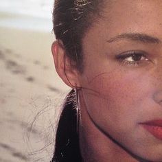 a woman with freckles on her face looking at the camera while standing in front of an ocean