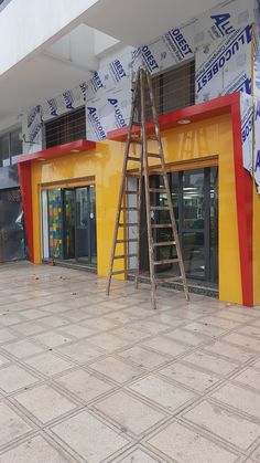 a ladder leaning up against a yellow and red building that has been painted with advertisements on it