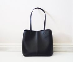 This simple tote features black vegan (fake) leather, magnet top closure and internal pockets. Details:-Dimensions: 12" length (top to bottom), 10" bottom width, 7" depth, 10" X 7" base (bottom)-Each shoulder strap measures approximately 23" full length-Black vegan (fake) leather-Fabric interior lining (solid black) - color can be customized-Internal pockets: 1 slip pocket, 1 zippered pocket-Magnet top closureBecause each bag is made by hand, the measurement is approximate and may vary slightly Medium Shoulder Bag With Large Capacity For Shopping, Sleek Tote Shoulder Bag For Daily Use, Everyday Bucket Bag With Magnetic Closure, Sleek Black Satchel For Everyday Use, Sleek Tote Satchel For Everyday Use, Sleek Satchel Tote For Everyday Use, Everyday Satchel Tote With Magnetic Closure, Everyday Satchel With Magnetic Closure And Tote Shape, Sleek Black Hobo Bag For Everyday