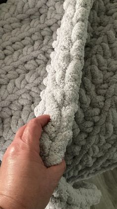 a hand is holding the edge of a gray and white knitted blanket that has been folded over