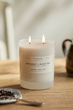 a lit candle sitting on top of a wooden table next to a tea cup and spoon