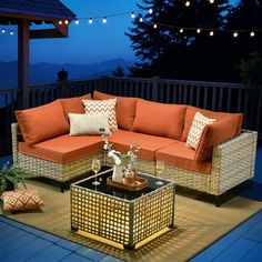 an outdoor living room with orange and white pillows on the couches, coffee table and string lights