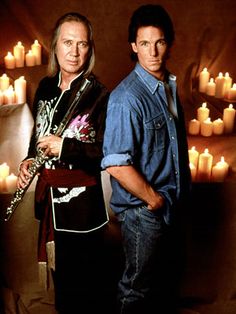 two men standing next to each other in front of candles with one holding a flute