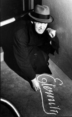 a man in a fedora is kneeling on the floor next to a chalk drawing