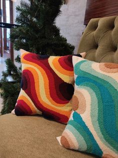 two colorful pillows sitting on top of a couch next to a christmas tree