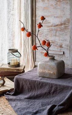 a vase filled with oranges sitting on top of a table next to a window