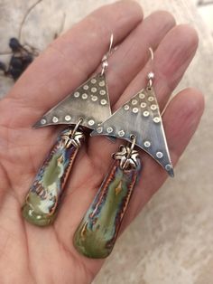 a pair of silver and green earrings on someone's left hand, in the shape of two triangulars