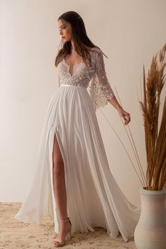 a woman in a white dress standing next to a vase with dried grass on it