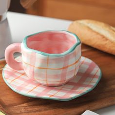 a pink and white checkered cup on a plate next to a loaf of bread