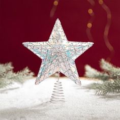 a glass star ornament on top of a tree in the snow with christmas lights behind it