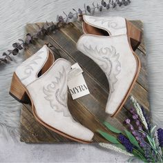 a pair of white cowboy boots sitting on top of a wooden table next to flowers