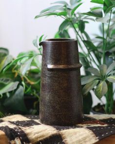 a brown vase sitting on top of a table next to a potted green plant