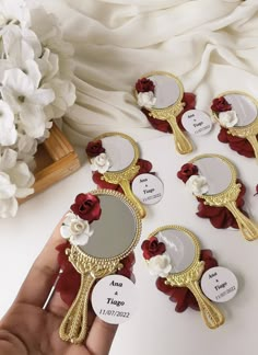 a hand holding a mirror with red flowers on it next to some white flowers and other items