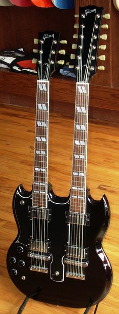 two electric guitars sitting on top of a hard wood floor next to each other in front of a shelf