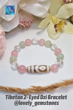 a bracelet with beads and charms on top of a table next to some pink flowers